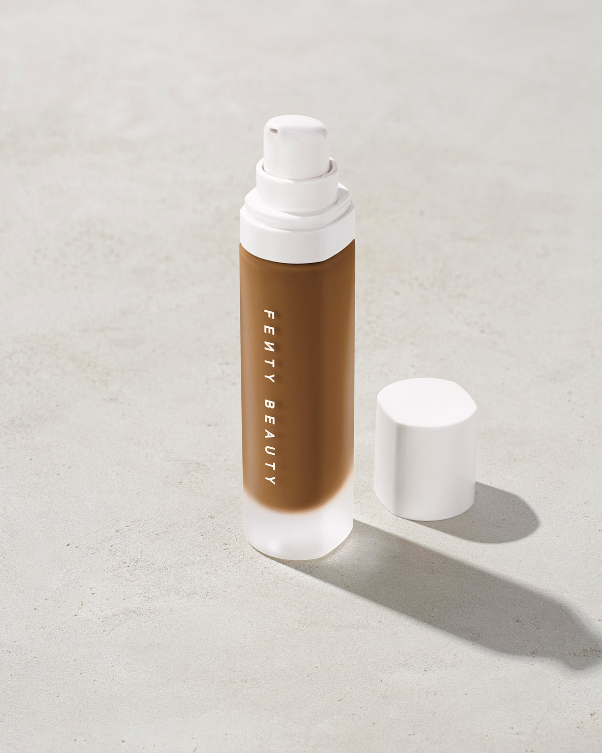 44763_Foundation_Concrete_Open_1200x1500_RGB_445 open bottle of Fenty Beauty Pro Filt'r Soft Matte Longwear Foundation with pump dispenser in shade 445 on concrete background