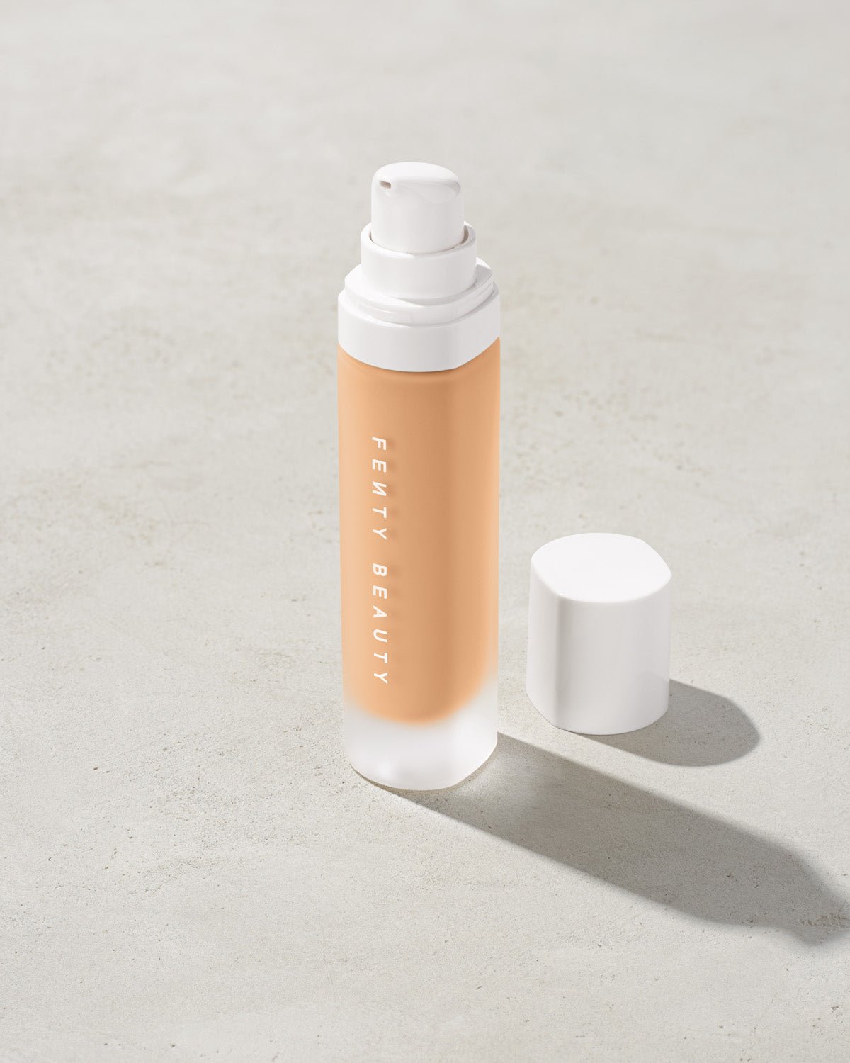 FB30006_FB0220_alt1 open bottle of Fenty Beauty Pro Filt'r Soft Matte Longwear Foundation with pump dispenser in shade #220 on concrete background