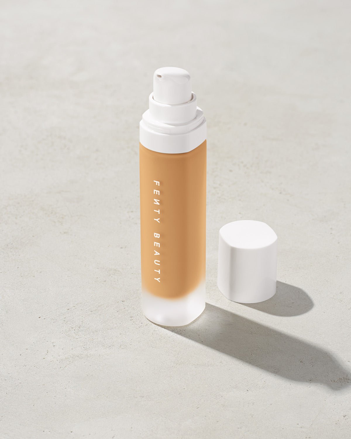FB30006_FB0290_alt1 open bottle of Fenty Beauty Pro Filt'r Soft Matte Longwear Foundation with pump dispenser in shade #290 on concrete background