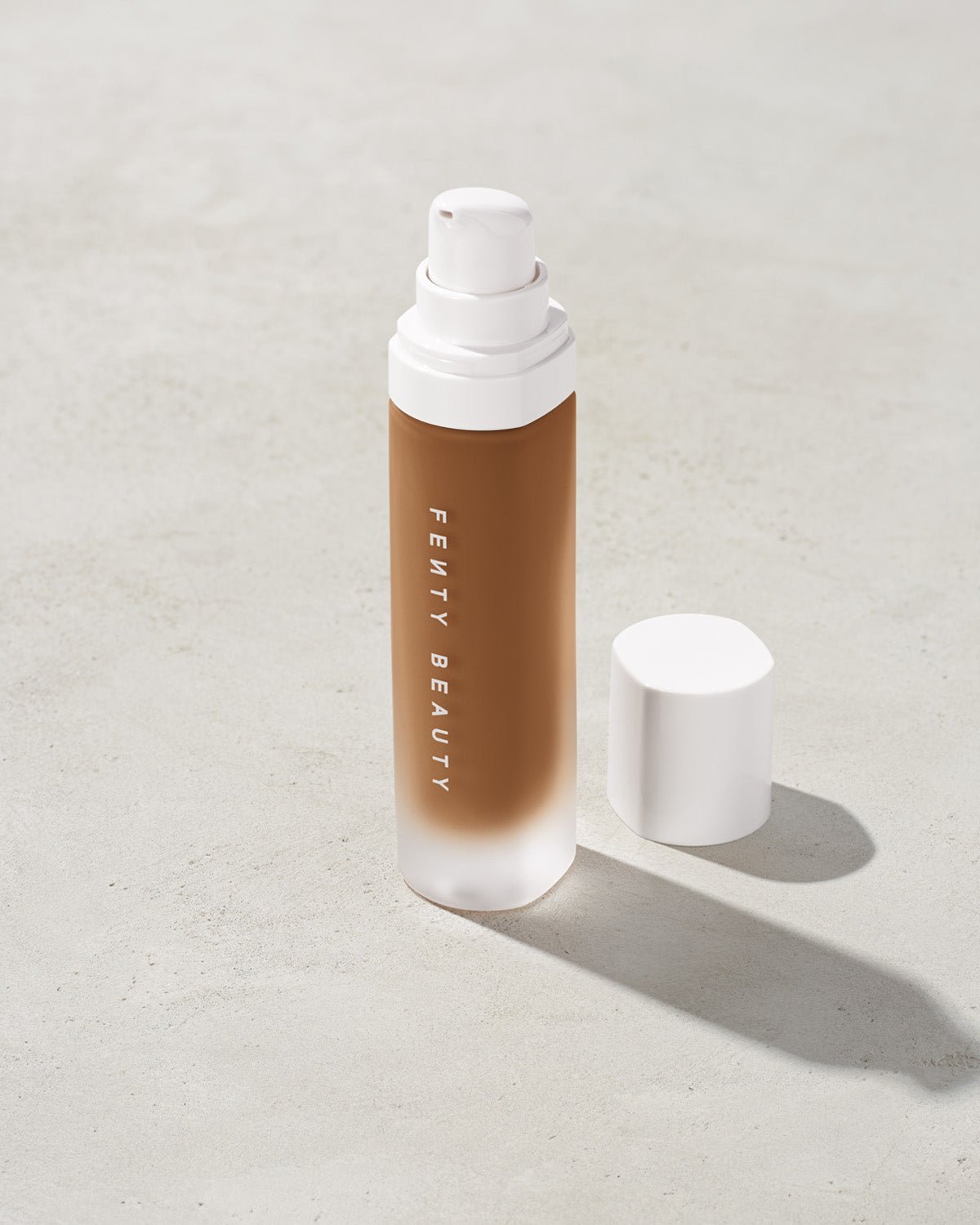 FB31006_FB0450_alt1 open bottle of Fenty Beauty Pro Filt'r Soft Matte Longwear Foundation with pump dispenser in shade 450 on concrete background