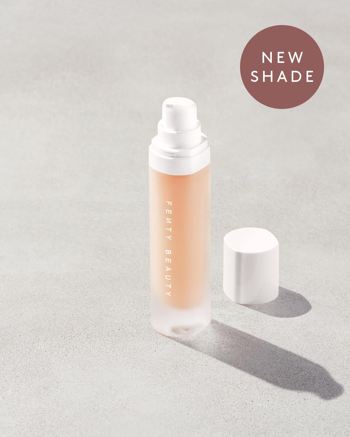 Open bottle of Fenty Beauty Pro Filt'r Soft Matte Longwear Foundation with pump dispenser in shade #125 on concrete background