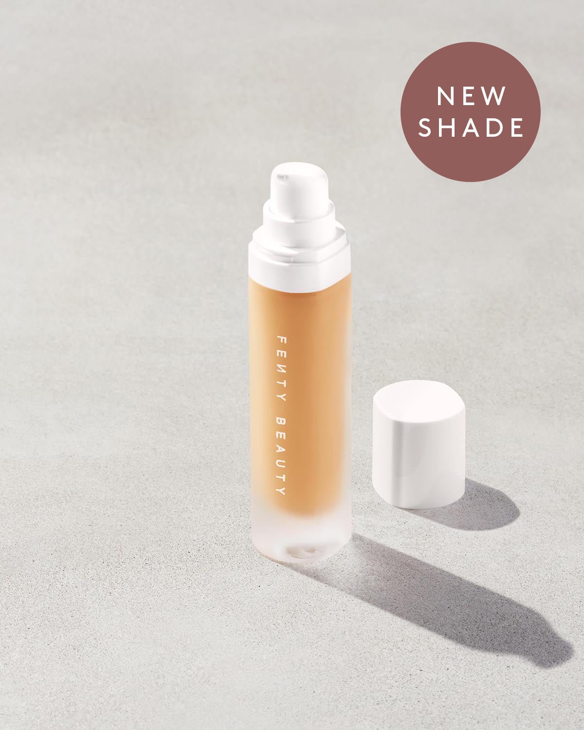 Open bottle of a new shade of Fenty Beauty Pro Filt'r Soft Matte Longwear Foundation with pump dispenser in shade #315 on concrete background