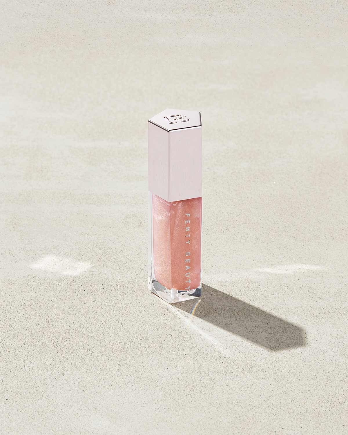 A closed tube of Gloss Bomb Universal Lip Luminizer in the shade $weet Mouth on a grey background.