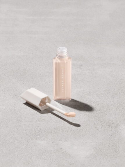Open bottle of Fenty Beauty We're Even Hydrating Longwear Concealer with doe foot applicator in shade 125c on a concrete background.