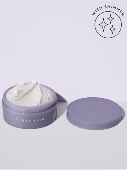 An open tub of Butta Drop Shimmering Whipped Oil Body Cream with Tropical Oils + Shea Butter on a lilac background and a badge on the top right that reads: with shimmer.