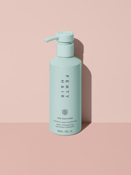 Fenty Hair The Rich One Moisture Repair Conditioner aluminum bottle with a pump on a pink background.